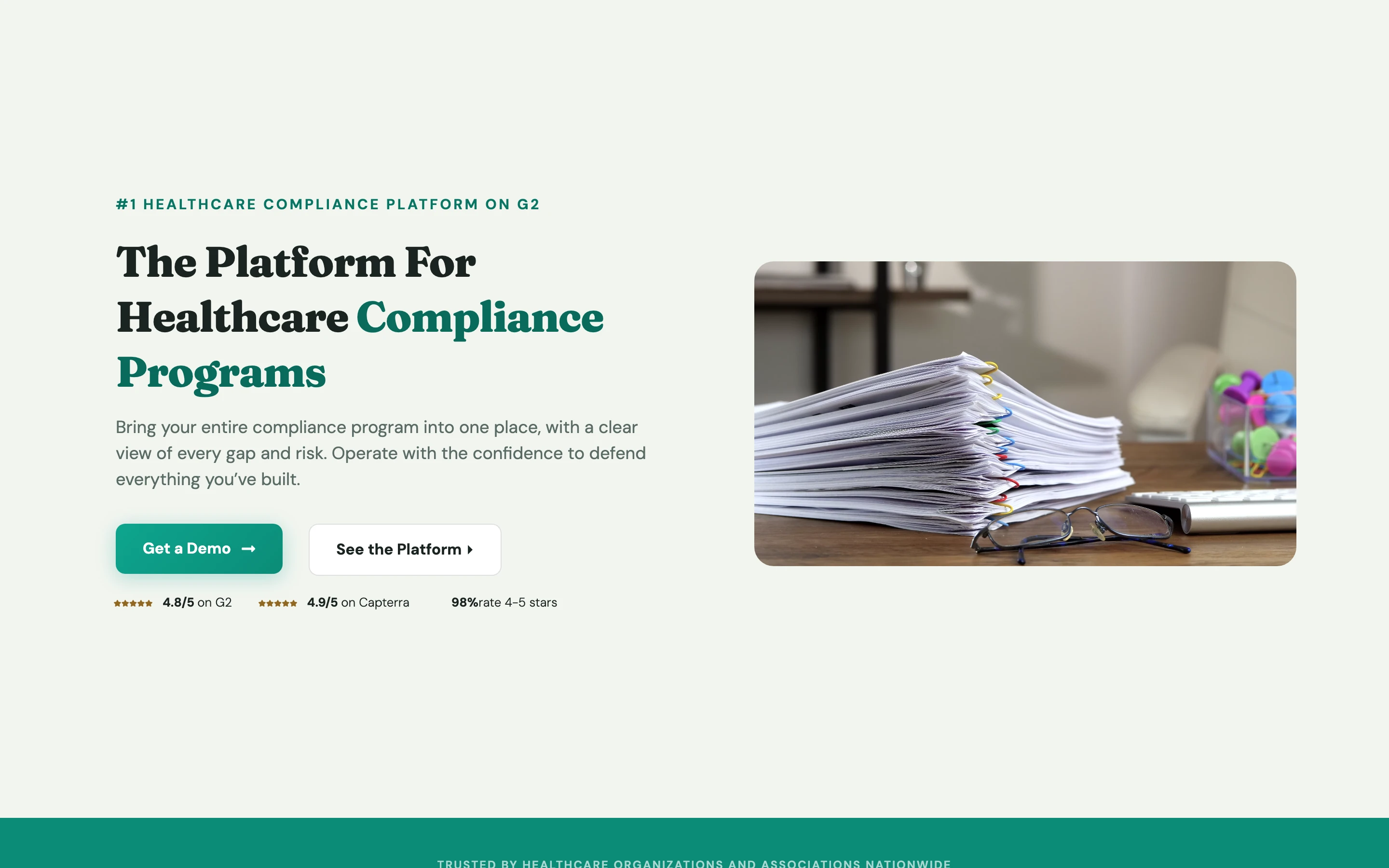 Compliancy Group 公式トップページの上部。「The Platform For Healthcare Compliance Programs」の見出しと、書類の束の写真、デモの申し込みボタン、G2 と Capterra の評価の表示